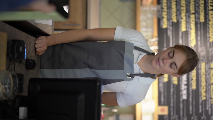 Smiling waitress barista saleswoman on coffee shop counter, woman client pay in cafe with phone via pos machine using nfc terminal make contactless mobile payment. | Shutterstock HD Video #1097266365