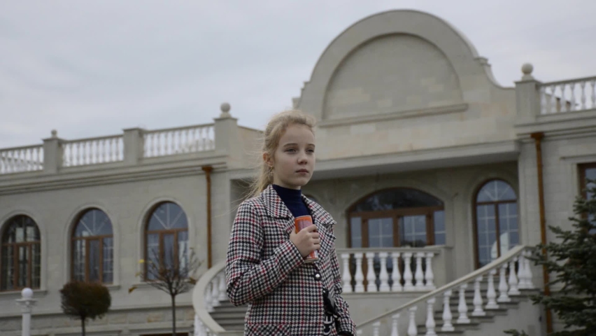 a beautiful girl in a flying coat smiles and waves her hand in greeting. the wind blows the child