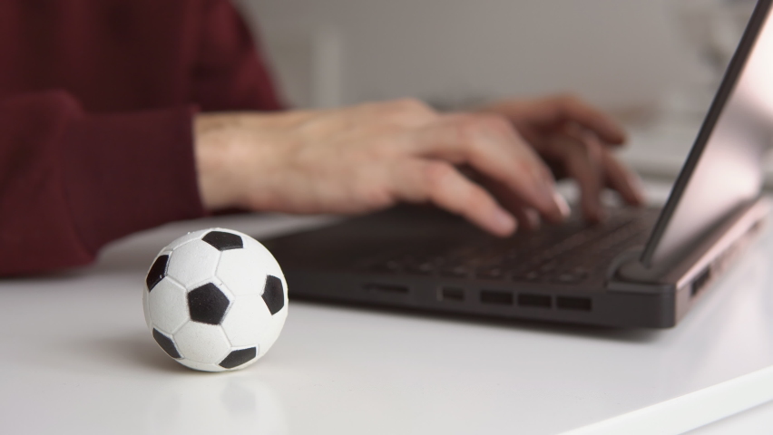 Young man reading soccer news or writing football article on laptop. Soccer ball on the table. Betting, gambling concept. | Shutterstock HD Video #1097270277