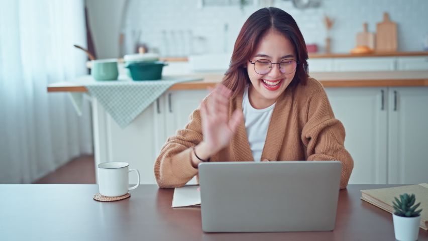 Happy positive young asian woman enjoying online communication at home, Female using wifi while video conferencing with friend, sitting in front of open laptop, smiling and waving hand, saying hi | Shutterstock HD Video #1097278029