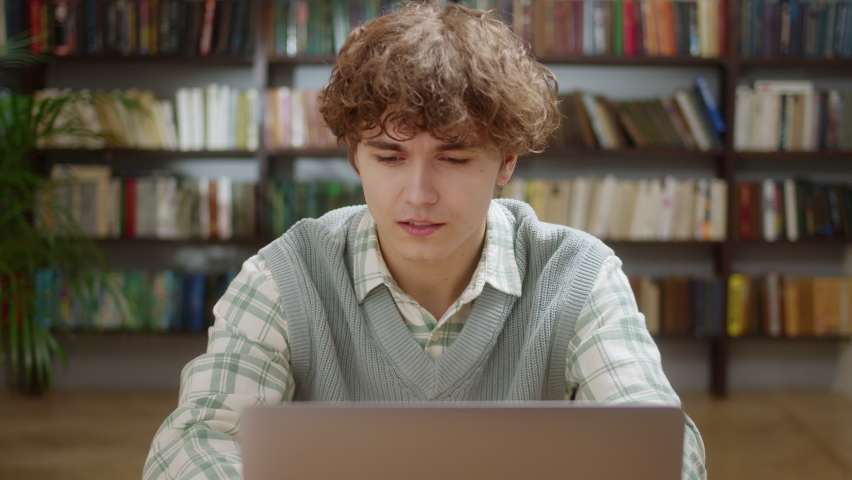 Attractive Student Curly Man Looking at Laptop Monitor Doing Research and Smile. Young Male Professional Using Computer and Smile Sitting at Home Office or Library. Busy Worker Freelancer Working on | Shutterstock HD Video #1097278975