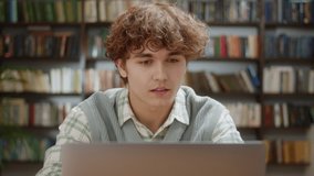 Attractive Student Curly Man Looking at Laptop Monitor Doing Research and Smile. Young Male Professional Using Computer and Smile Sitting at Home Office or Library. Busy Worker Freelancer Working on