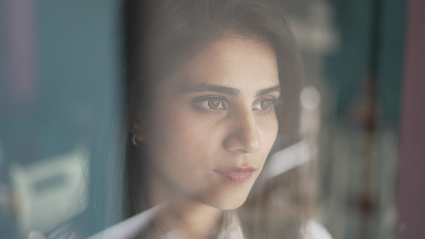 Close up view of Pensive worried young Indian woman looking outside through window. Thoughtful serious Asian girl feeling sad or melancholic, reflecting alone,thinking or loneliness in coffee cafe. | Shutterstock HD Video #1097280139
