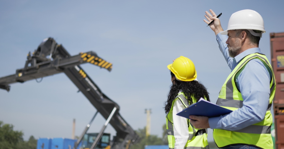 Caucasian Engineer man and female foreman worker wearing helmet and safety vest control loading a shipping Container, use hand signal while lifting containers box from cargo, Logistic concept