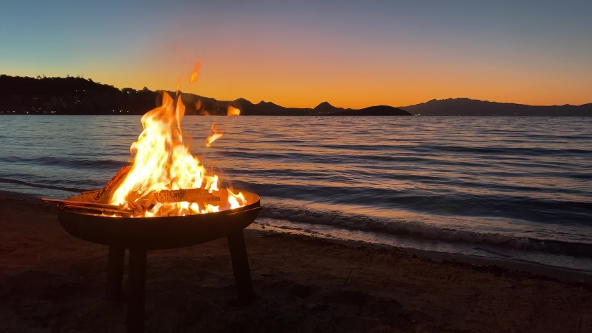 Beautiful sunset and sea view with Burning fire pit at beach. Happy weekend campfire activity. Cozy beach party with fireplace. Romantic vacation background in slow motion with copy space. Royalty-Free Stock Footage #1097281243