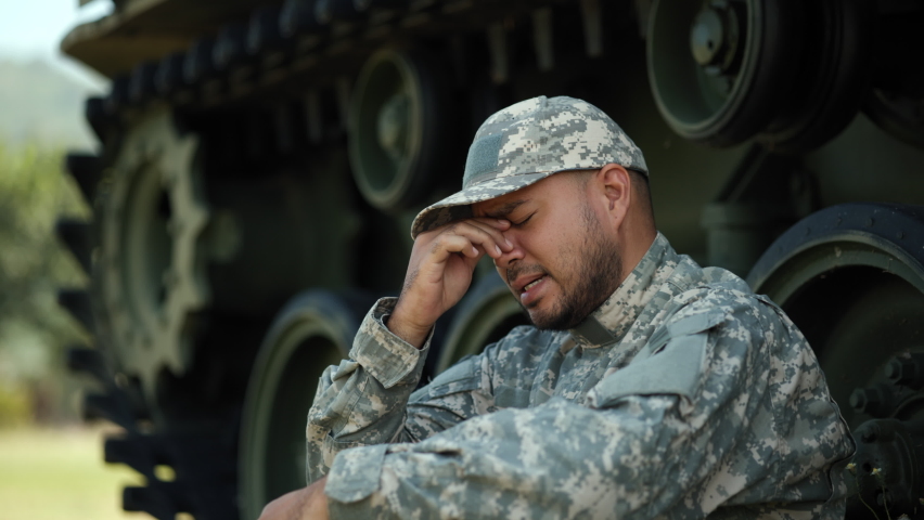Crying soldier man in military uniform special forces standing against on field Mission lose war. Commander Army soldier defender of nation in uniform siting near battle tank while state of war.