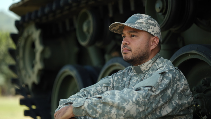 Commander Army soldier military defender of nation in uniform siting near battle tank while state of war. Serious man in military uniform special forces soldier standing against on field Mission.