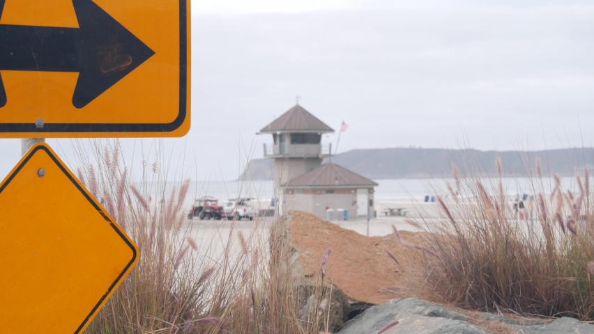 Lifeguard stand or life guard tower hut, surfing safety on California beach, USA. Rescue station, coast lifesavers wachtower or house, Coronado ocean beach, San Diego. Yellow arrow road sign and cars.