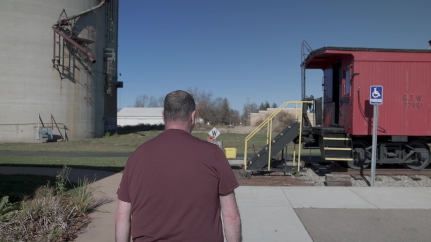 Man walking to antique red caboose with gimbal video walking behind.