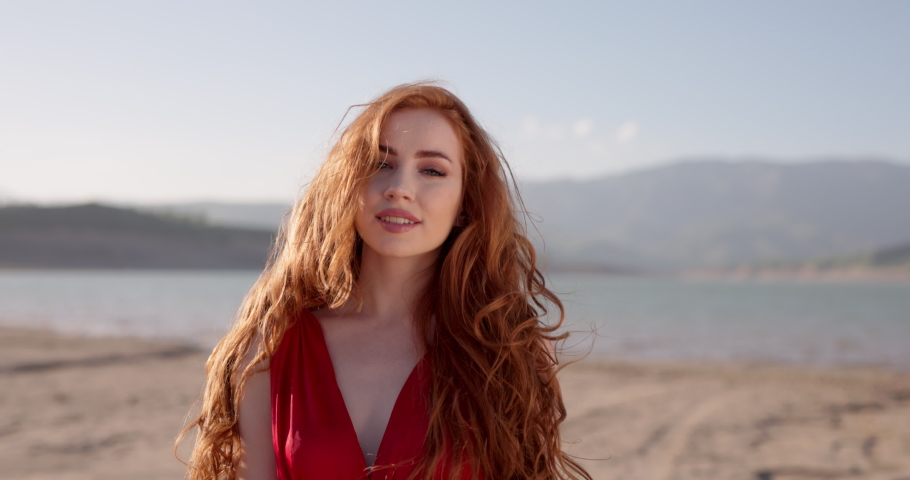 Redhead Female Wearing Red Dress on Beautiful Landscape Waving Hand, Inviting to Follow Her. Gorgeous Woman with Long Curly Hair Looking at Camera, Positively Smiling. Slow motion. Trust Concept | Shutterstock HD Video #1097288365