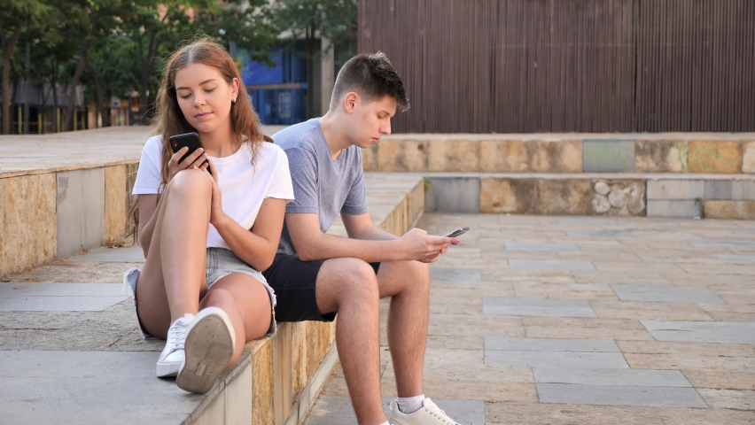 A coulpe of teenagers with smartphones is sitting on the step 