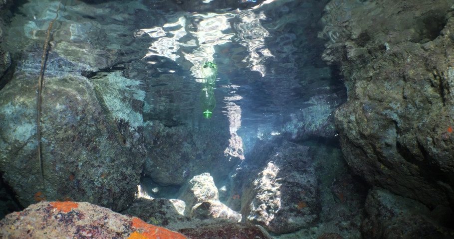 A green plastic bottle in a cave underwater ocean pollution with sun beams and rays | Shutterstock HD Video #1097292159