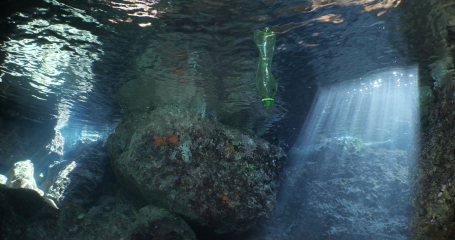 A green plastic bottle in a cave underwater ocean pollution with sun beams and rays | Shutterstock HD Video #1097292165