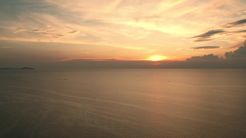 Beautiful sunset on coastline tropical beach with golden sea and silhouette travel people on nature background, Ocean sunset timelapse, fly in clouds, sun going beyond the horizon illuminating water