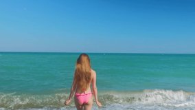 Tall woman with a long hair from a back is on a beach. Mediterranean sea with waves on the background. Blue and turquoise water. Vacation summer vibe. Slow motion video. 