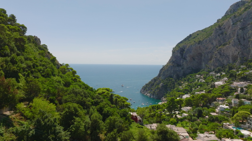 Forwards fly above lush green vegetation. Revealing panoramic view of attractive tourist destination at sea coast. Capri, Campania, Italy Royalty-Free Stock Footage #1097298469