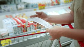 Woman checks paper check after shopping for groceries at mall by checking Dear Amount bill in a grocery cart. increase in food prices, spending money in hypermarket. Woman checking grocery store cart - Powered by Shutterstock - Get 15% off with code: PIKWIZARD15