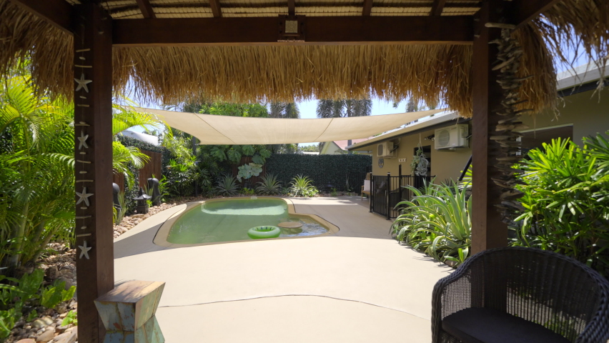 Bali style Pool hut gazebo lounge deck. Temples and buddha statue feature. Luxurious outdoor pool with elegant pool stone coping tiled stone. Tropical garden green palm trees. Shade sail palm trees