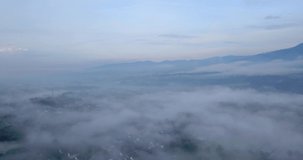 Drone footage flyover sea of fog above urban areas - Tropical city in Indonesia