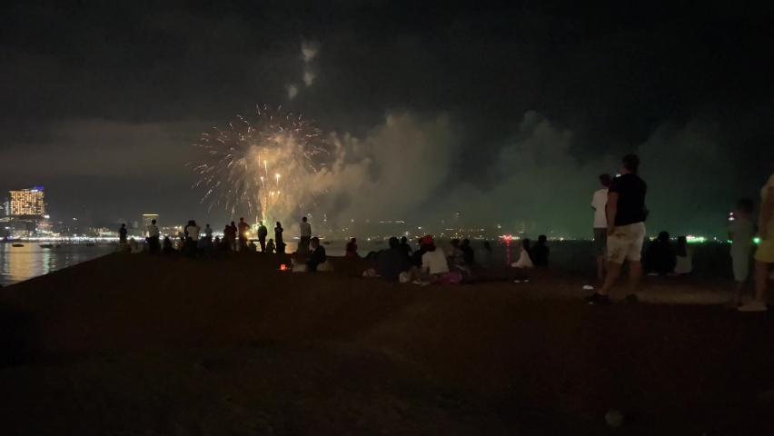 Fireworks show at Pattaya Fireworks Festival at night. View of people gathered on beachfront enjoy and watch beautiful glowing fireworks. Celebration and festivity concept