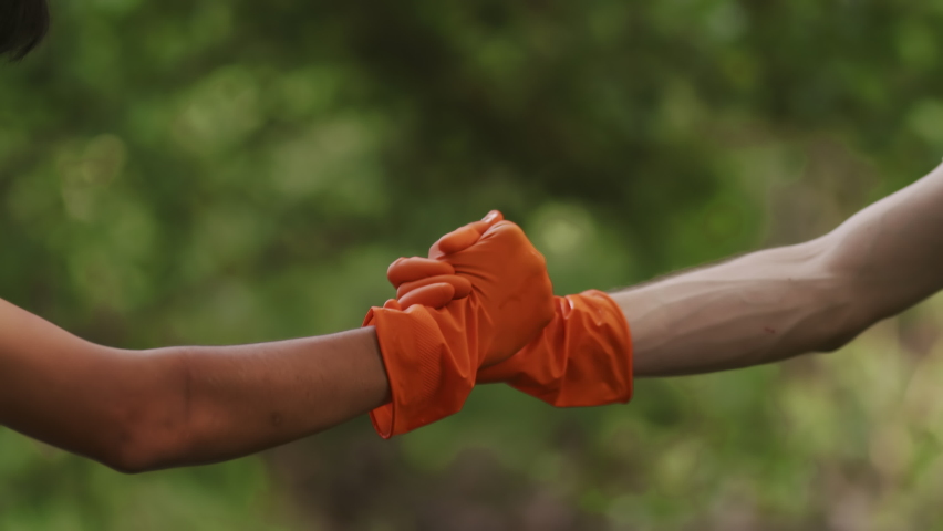Young ecological volunteers shaking hands in gloves in the forest. Young men enjoying environment care and volunteer teamwork outdoor | Shutterstock HD Video #1097305947