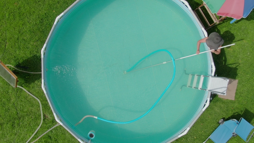 Aerial view on the woman in a hat cleaning the pool with a water vacuum cleaner on the backyard | Shutterstock HD Video #1097308181