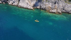 Young woman on a stand up paddle board SUP rawing among beatyful rocks. Clear blue sea water surrounds her. Aerial slowmotion video