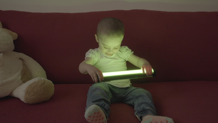 Caucasian little girl plays on the red sofa with a led lamp
