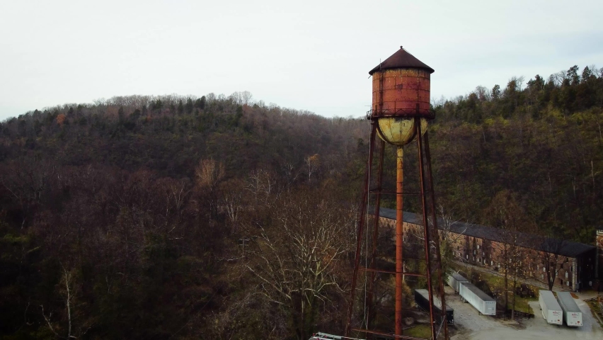 Approaching old, rusted water pressure reservoir tower, continue along bourbon aging warehouses next to distillery in rural Kentucky