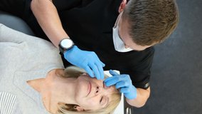 Vertical video, a surgeon examines the face of an old woman with his hands for plastic surgery.