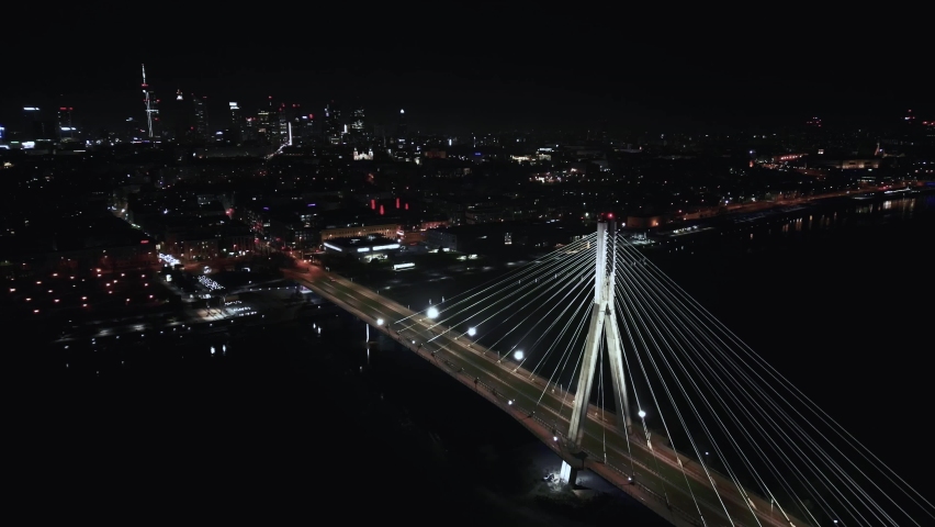 Scenic aerial view of night car traffic on illuminated suspension bridge with Warsaw in 4K urban cityscape, advanced innovation, financial technology Warsaw. Poland