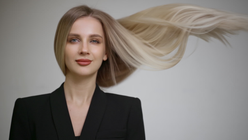 Slow motion of the flying hair of a charming blonde. Grey background.