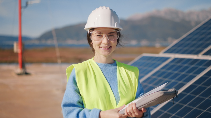Female young inspector portrait in protective vest and helmet check solar panel. Woman engineer builder inspect weather station efficiency make notes. Energetics, engineering modern technology concept Royalty-Free Stock Footage #1097323165