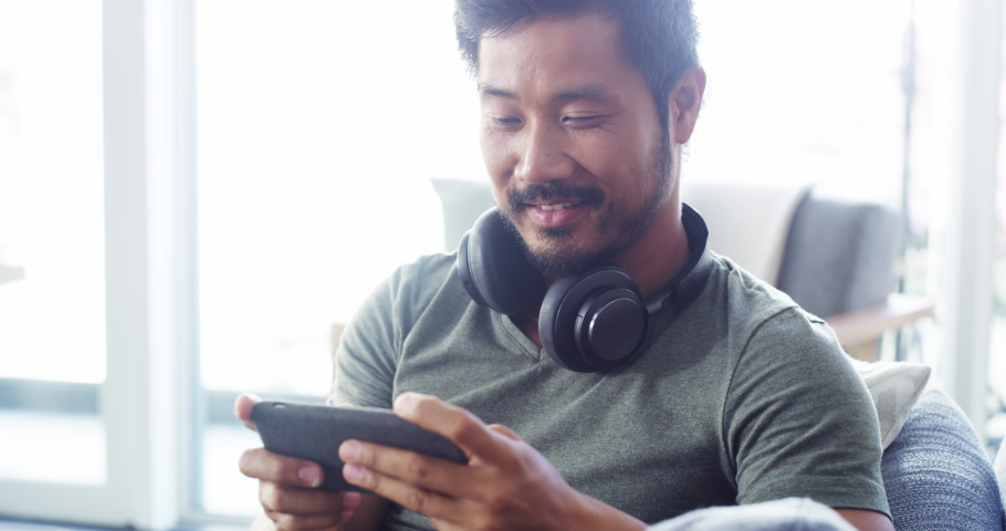 Asian man, gamer and relax with phone on sofa playing video games, streaming movies or entertainment at home. Man smiling relaxing on living room couch enjoying wireless mobile gaming on smartphone | Shutterstock HD Video #1097324997