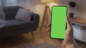 Handheld Camera: Point of View of Man on Living Room at Night Holding Chroma Key Green Screen Smartphone Watching Content Without Touching or Swiping. Boy Using Mobile Phone, Browsing Internet