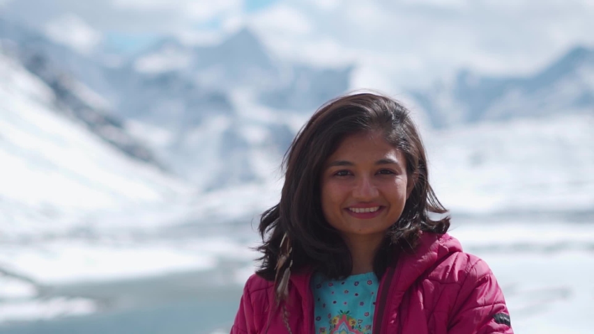 Portrait of Indian tourist girl in snow covered mountains looking at camera at Shinku La Pass, India. Winter holiday concept. Beautiful woman in background of snowy mountains during winter day. | Shutterstock HD Video #1097332423
