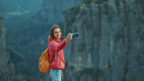 girl hiker takes selfie or video call on her smartphone on Tazi Canyon background. Happy woman on top of cliff enjoying mountain view, hike in famous touristic place in Turkey.
