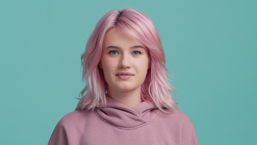 Portrait of fun scared young pretty hipster student 20s with pastel pink hair color in hoodie on isolated blue studio background 4K. Nervous young woman feeling panic, feeling worried and confused Royalty-Free Stock Footage #1097355193
