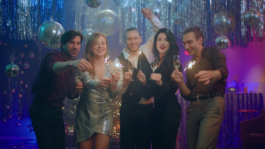 Handsome guys and two beautiful ladies celebrating the New Year in the club they holding champagne glasses the sparkles in front of the camera dancing and enjoy the night out Royalty-Free Stock Footage #1097356901