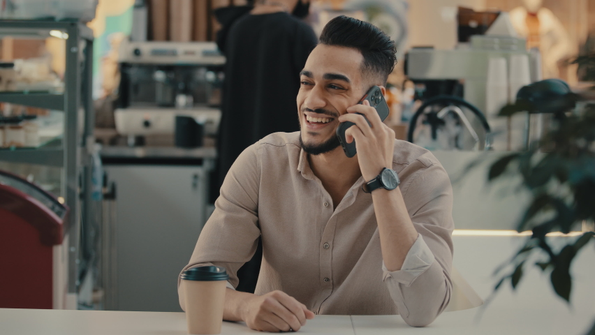 30s happy smiling laughing bearded Indian Hispanic ethnic man multiracial businessman worker entrepreneur employer sitting at cafe table talking mobile phone speak with smartphone talk with cellphone  | Shutterstock HD Video #1097360675
