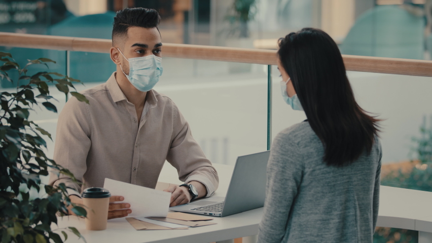 Bank worker in medical mask businessman salesman insurance man realtor manager talking with female client woman advises financial consultation with papers sells auto real estate girl signs contract | Shutterstock HD Video #1097360697