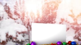 Animation of snow falling over white card with copy space and christmas decoration in winter scenery. Christmas, festivity, celebration and tradition concept digitally generated video.