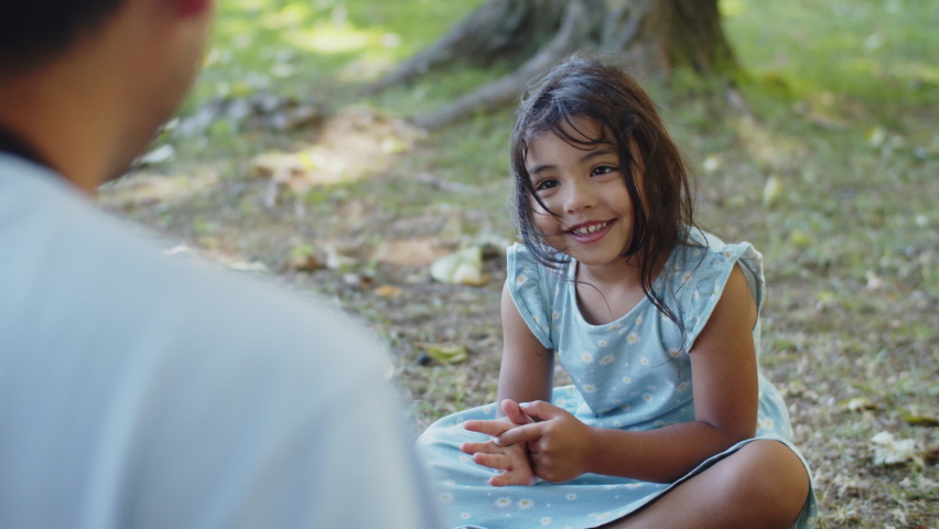 Happy Asian girl sitting on ground while father taking photo with camera. Toddler daughter wearing blue dress looking at camera and smiling. Fatherhood and childhood concept