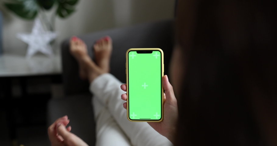 Young woman using mobile phone with green screen for copy space closeup. Chroma key mockup on smartphone in hand. Person holds cellphone and swipes photos or pictures indoors at home | Shutterstock HD Video #1097368677
