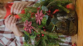 Young woman florist making Christmas flower arrangement. Vertical video. Small business concept.