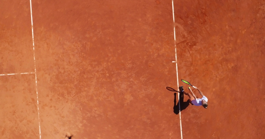 Aerial top view of a young female tennis player playing on brown ground court. Professional girl tennis player hitting a backhand on court Flat layout sport background. 