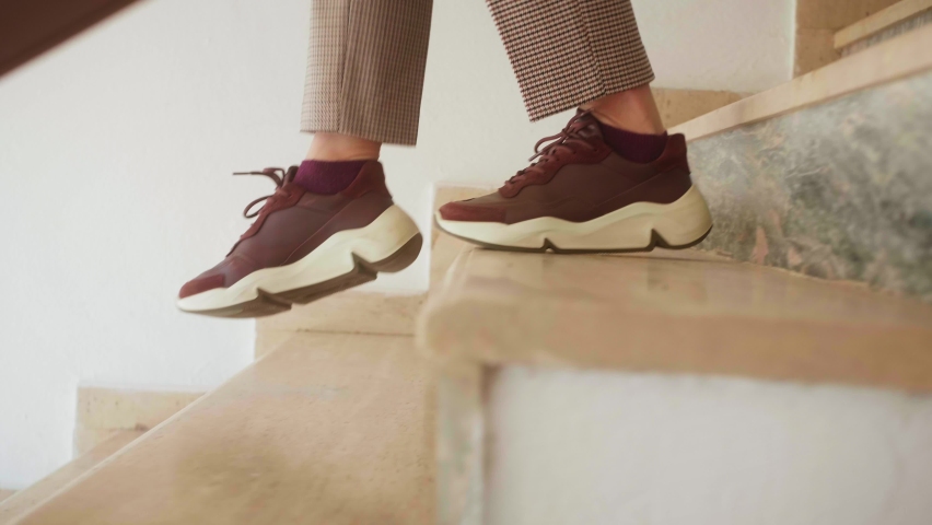 Woman in casual clothes goes down stairs. Close up of legs stepping down stairs.