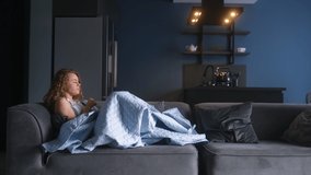 Woman sick with flu coughing and blowing her nose under blanket on couch at home. Young caucasian female suffering from coronavirus Covid19 while isolating. Ill girl laying on a sofa struggling cold - Powered by Shutterstock - Get 15% off with code: PIKWIZARD15