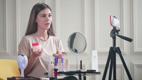 Beauty blogger sharing her impressions of a cosmetic product and giving some advice to the subscribers. Girl recording vlog using smartphone on tripod