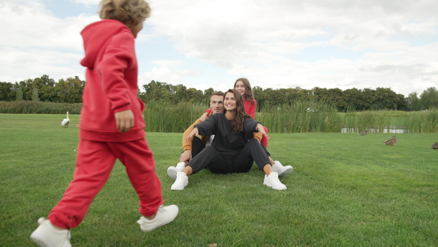 Lifestyle child runs up and hugs his parents and sister. A happy family together on a walk in the park laughs, fools and rejoices together. High quality 4k footage